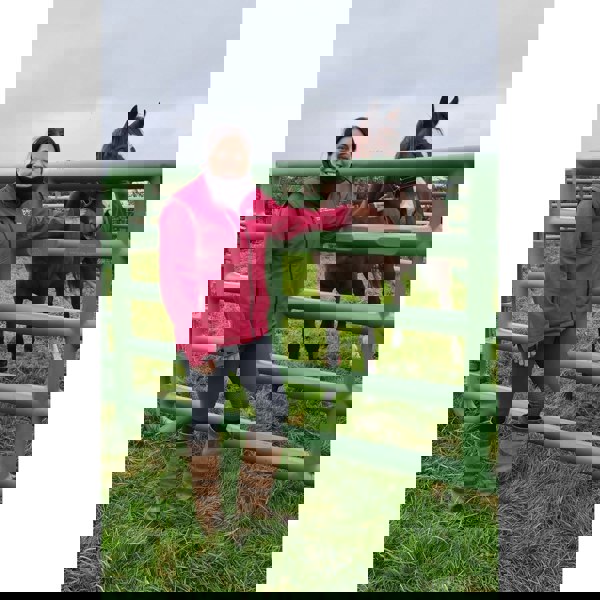 Ruffnek black fleece neck warmer neck gaiter shown worn by a horse woman stood next to a horse in a livery yard.