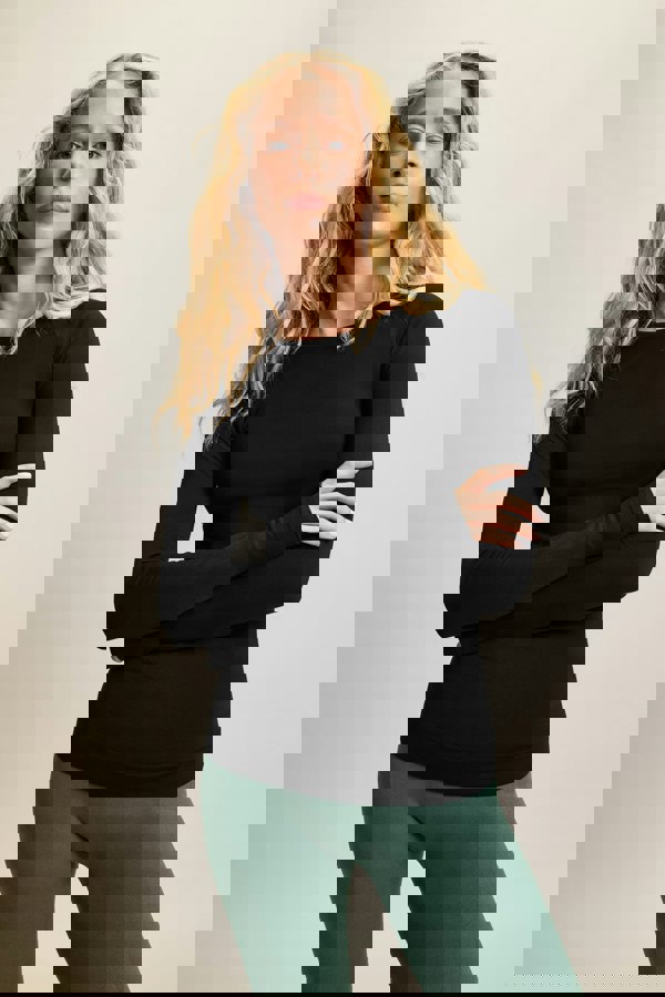 Model wearing a black long-sleeve top made from moisture-wicking fabric, paired with high-waisted green leggings. The sleek, seamless design of the lightweight and breathable long-sleeve top, featuring thumbholes, makes it perfect for yoga and athleisure wear. Ideal for activewear enthusiasts seeking stylish and sustainable workout gear, this outfit combines high-performance sportswear with versatile, all-day comfort. Suitable for a variety of activities, from intense workouts to casual athleisure looks