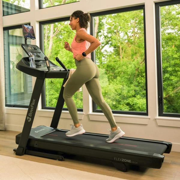 Woman running on a BowFlex T6 treadmill in a bright home gym setting.