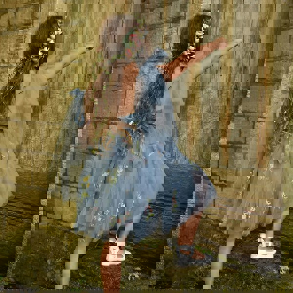 Young girl in a blue floral dress standing against a rustic stone wall.