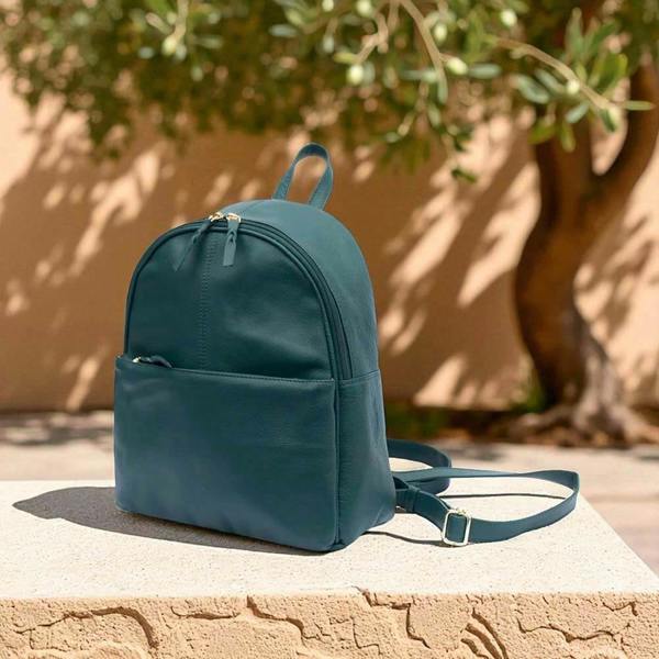 Teal backpack on a stone surface with a beige wall and tree in the background