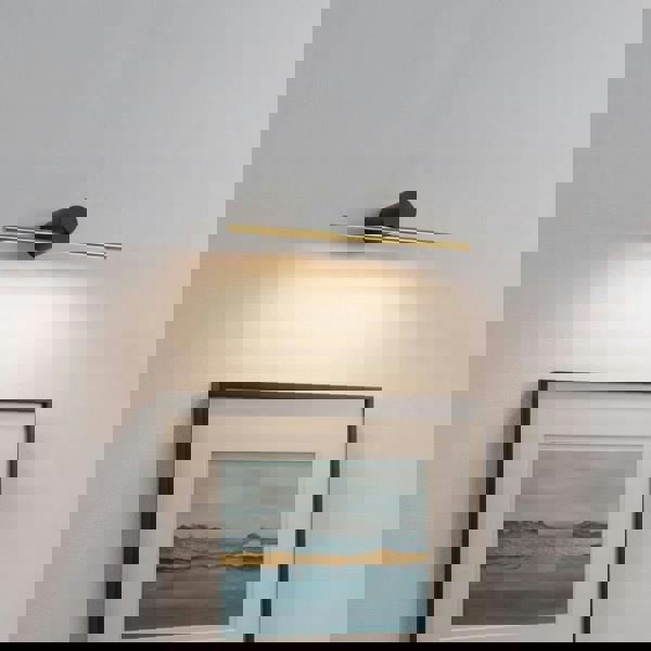 gold picture light mounted on the wall over artwork 