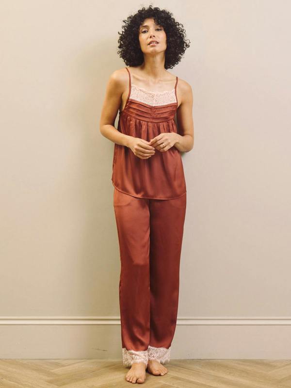 Woman wearing a rust-coloured pyjama set with lace trim against a beige wall.