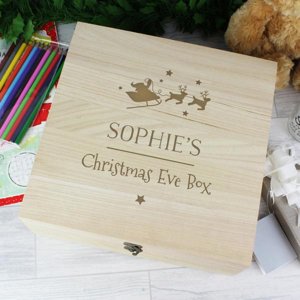 A top-down view of a light timber Personalised Large Wooden Christmas Eve Box engraved with Sophie's Christmas Eve Box and a Santa sleigh motif, next to coloring pencils.