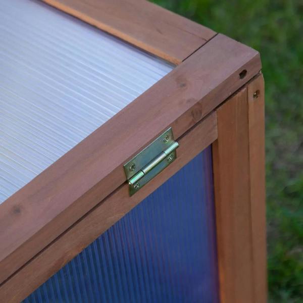 Metal hinge detail on a wooden cold frame lid with clear polycarbonate glazing
