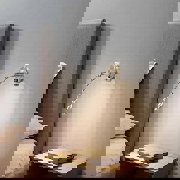 Antique finish flexible bedside reading light mounted on the wall next to a bed and over a bedside table 