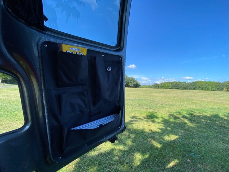 An image of the right hand side of the VW T5/T6 Barn Door Storage Organiser with some items stowed inside of it being used on a campsite.