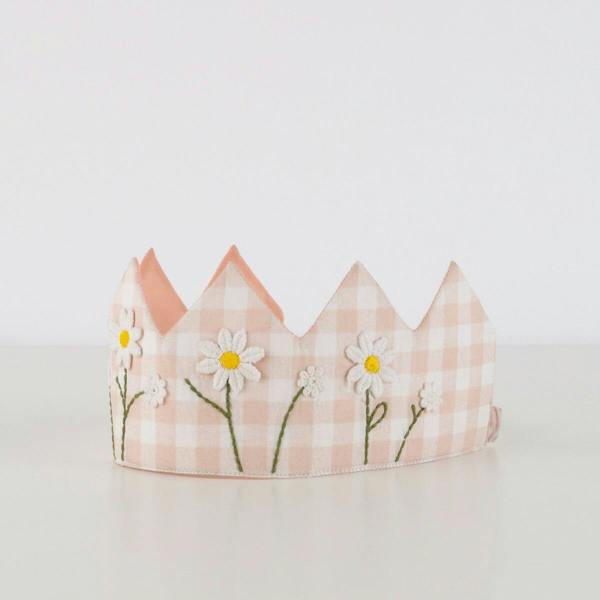 A studio product shot of the pink and white gingham fabric crown showing its embroidered daisies standing upright against a plain white background.