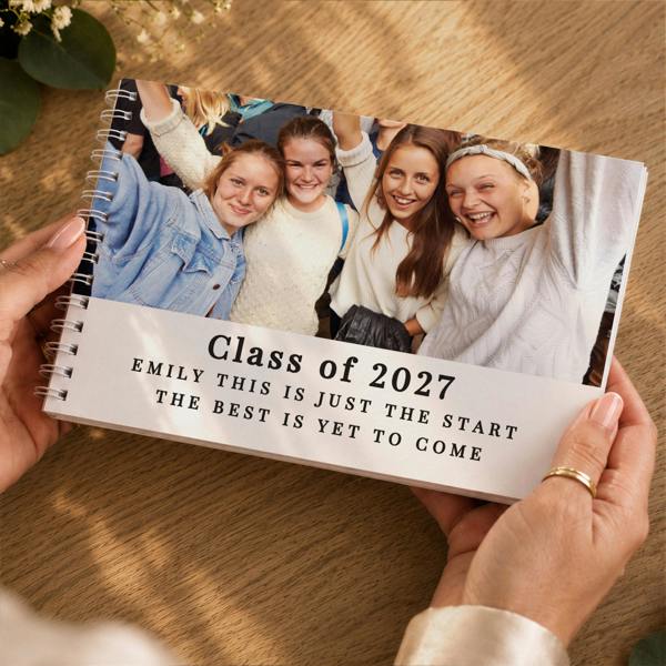 Hands holding the Personalised Photo Upload Guest Book featuring a group photo of friends and Class of 2027 graduation text by Abode Home & Gifts
