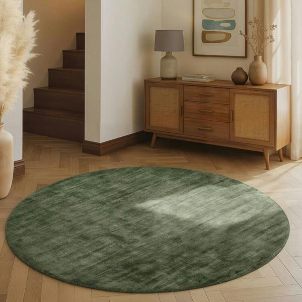 Round green rug on a wooden floor with a wooden sideboard and decor in the background.