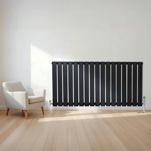 Flat black single column radiator with sleek vertical slats, paired with chrome valves, positioned beside a modern armchair in a bright room