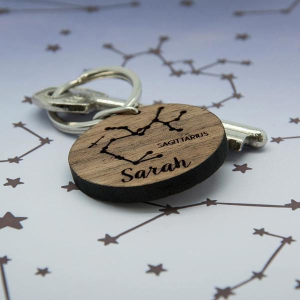 Angled close-up of a personalised walnut wooden zodiac keyring showing the engraved Sagittarius constellation, name Sarah, and natural wood edge.