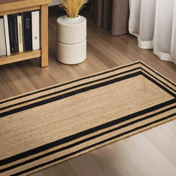 Beige rug with black stripes on a wooden floor, next to a bookshelf and plant.