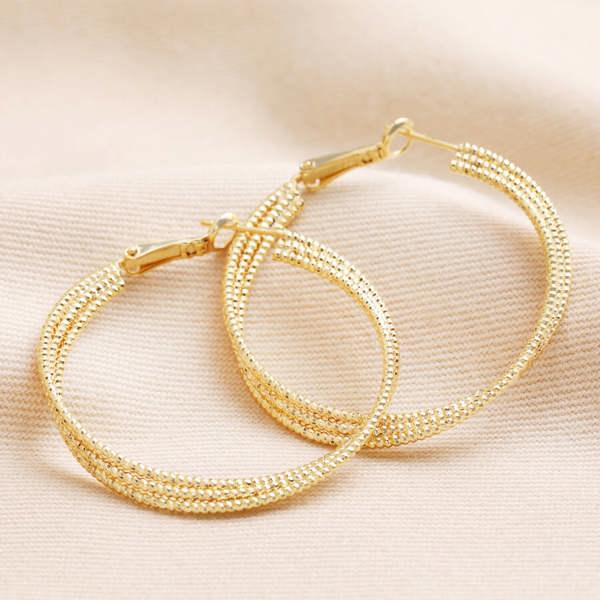 Pair of gold triple-layered thread hoop earrings on a light beige fabric surface
