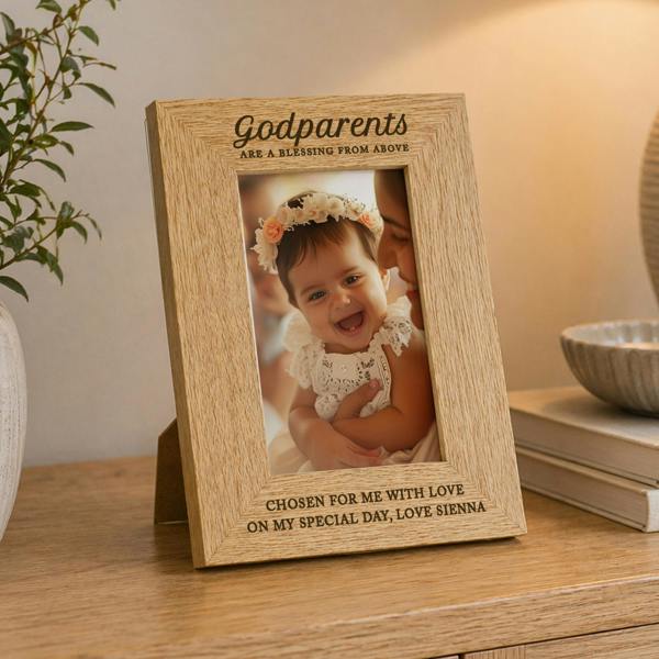 An engraved oak veneer picture frame holding a portrait photo of a smiling young child, styled on a wooden tabletop next to books.