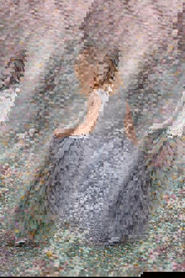 Young girl in a white top and gray ruffled skirt standing in a field of flowers.