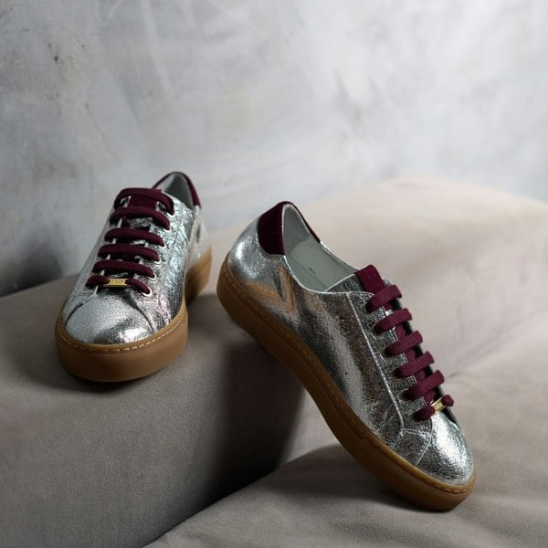 Silver sneakers with maroon laces on a light gray surface