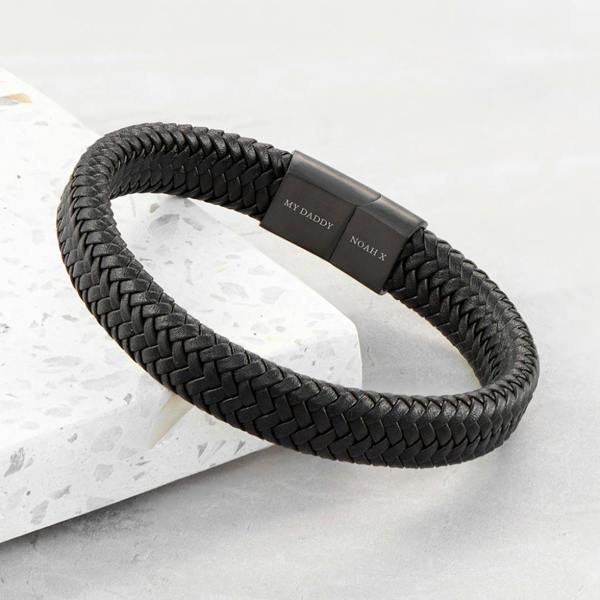 Personalised men's black braided leather bracelet featuring a matte black clasp engraved with 'MY DADDY' and 'NOAH X'.