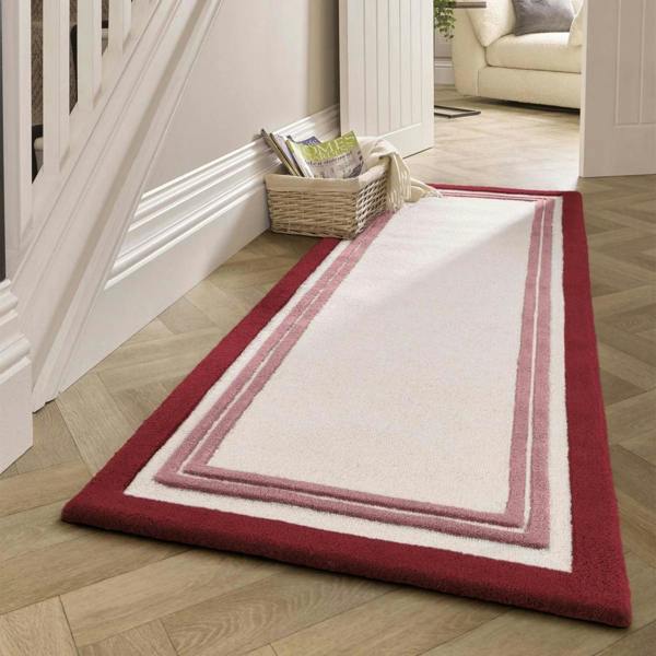 White rug with red border on a wooden floor next to a staircase