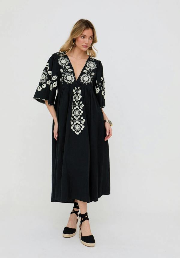 Woman wearing a black dress with white embroidery on a white background