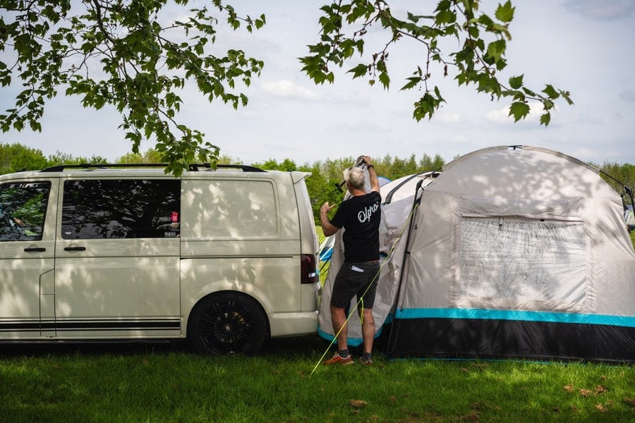 A man sets up the Snug Poled Tailgate Awning on a Volkswagen T5