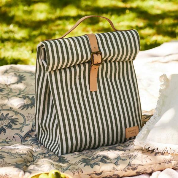 Moss green striped folding lunch bag with a tan buckle strap sitting on a patterned cushion.
