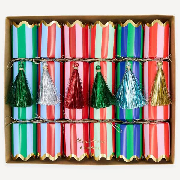 Top-down studio shot of six colourful striped Christmas crackers with shimmering tinsel tassels arranged neatly inside a brown gift box.