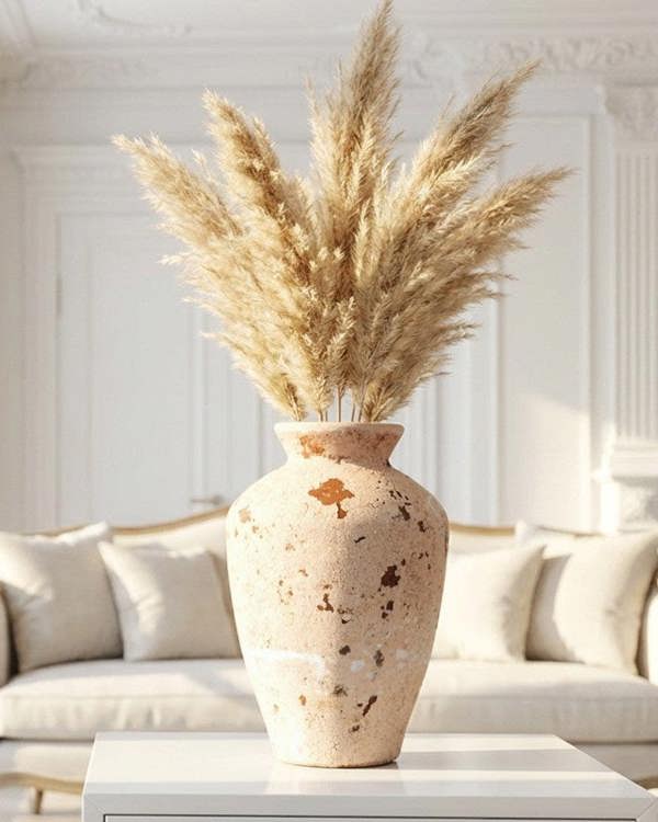 Decorative vase with dried pampas grass on a white surface in a bright room.