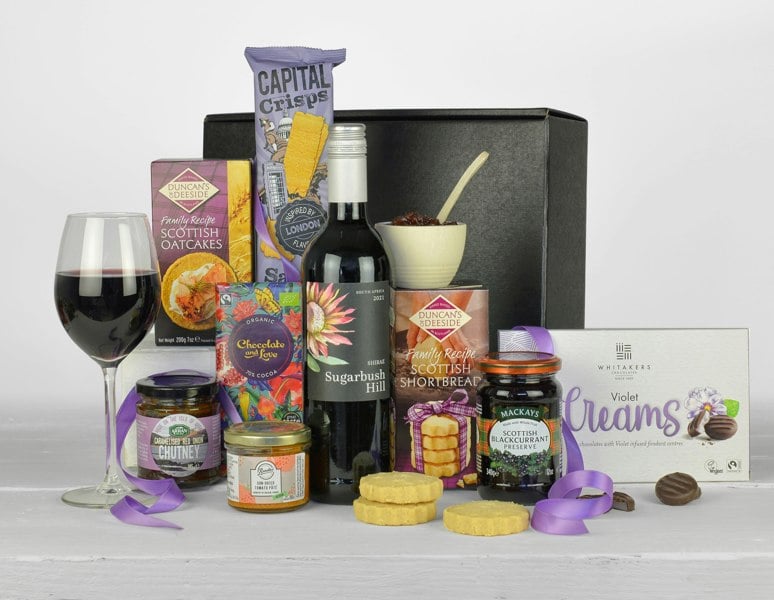 a bottle of red wine and tasty treats that are purple in colour and are all Vegan in a black gift box