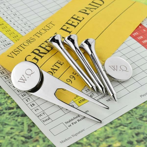 Three shiny silver-plated golf tees and a silver divot repair tool with a round ball marker engraved with the initials 'W.Q', arranged over a yellow green fee visitors ticket and score card.