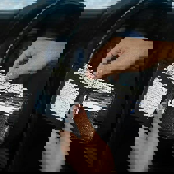 Person holding a black wallet with money and cards inside, sitting in a car.