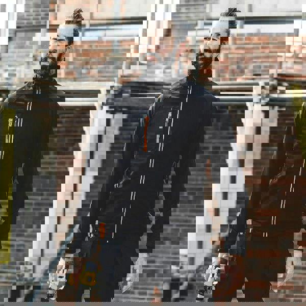 Scruffs Trade Flex Softshell Mens Zip Up Work Warm Jacket Coat, a man wearing a black zip-up softshell jacket with multiple pockets, standing at a construction site.