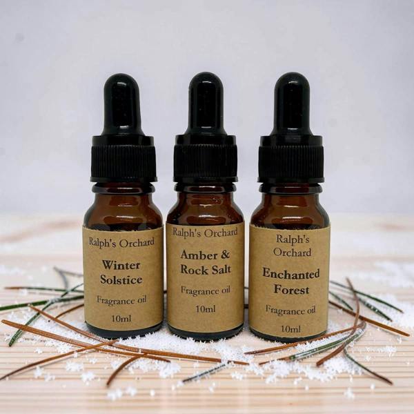 Three bottles of Ralph's Orchard fragrance oils on a wooden surface with decorative elements.