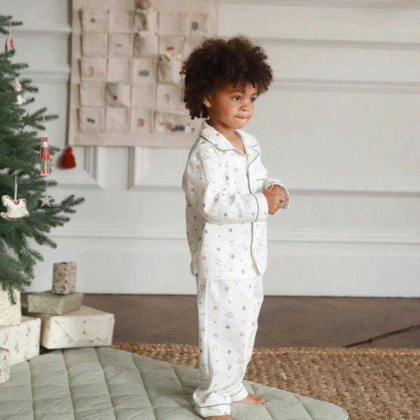 A young boy standing in profile next to a Christmas tree, wearing traditional white organic cotton flannel pyjamas with a Nutcracker print.