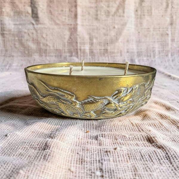 Decorative candle in a brass holder with embossed design on a textured fabric background