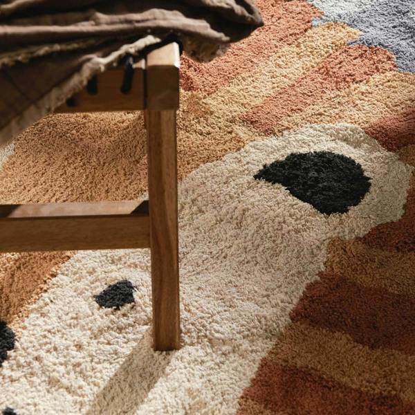 Close-up of a textured rug with geometric patterns and a wooden chair leg.