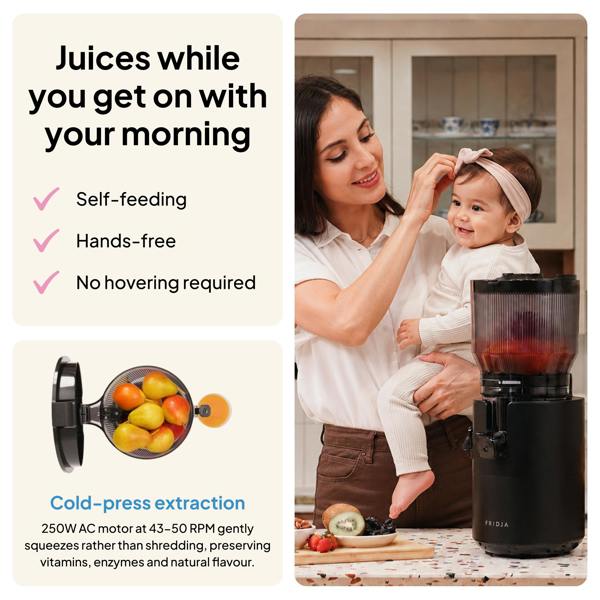 A smiling woman prepares her baby with the Fridja f2800 Open Whole Fruit Juicer, packed with fruit. Features include: “Juices while you get on with your morning,” “Self-feeding hopper,” “Hands-free,” and cold-press extraction.