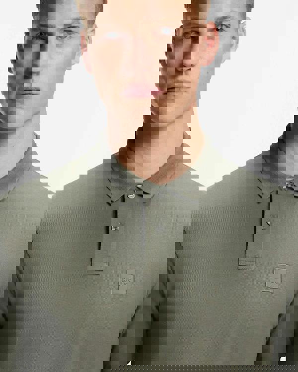 Man wearing a green polo shirt with a BOSS logo on a white background