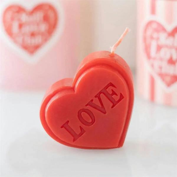 Red heart-shaped candle with LOVE embossed and lit wick
