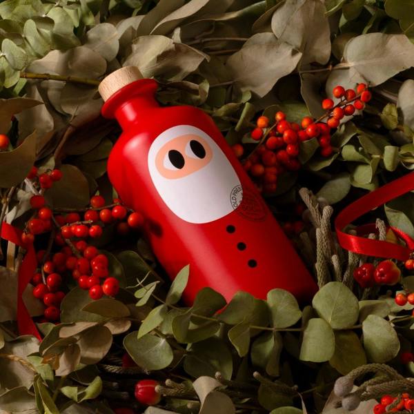 Festive flat-lay featuring the 500ml Santa edition extra virgin olive oil bottle nestled among eucalyptus leaves, red winter berries, and ribbon.
