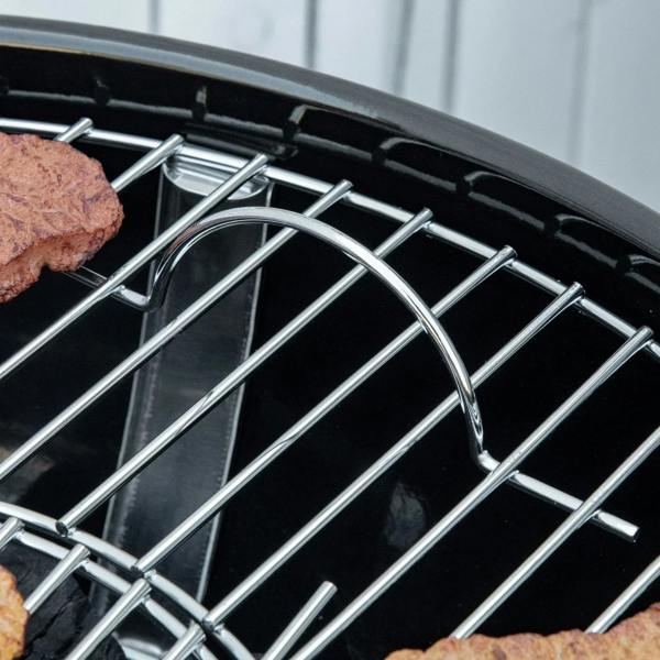 Stainless cooking grate inside black kettle charcoal grill with patties and coals visible.