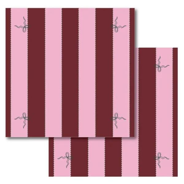 A studio product image showing a set of two square cloth napkins featuring a bold burgundy and pink stripe pattern with small embroidered bows.