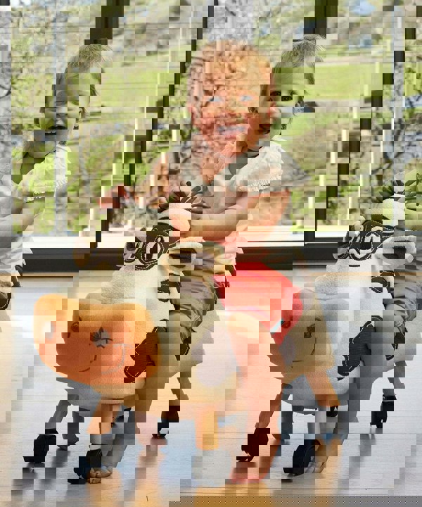 Little girl riding Moobert Cow Ride On Toy on wooden floor