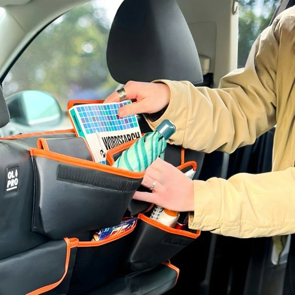 An adult male retrieving a word search from the OLPRO Rear Double Seat Storage Organiser in orange that is full of dog walking items and attached to the back of the rear seats of a VW vehicle.