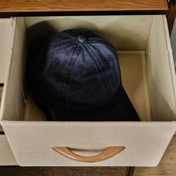 Fabric drawer compartment holding a dark baseball cap, with wooden pull handle on dresser