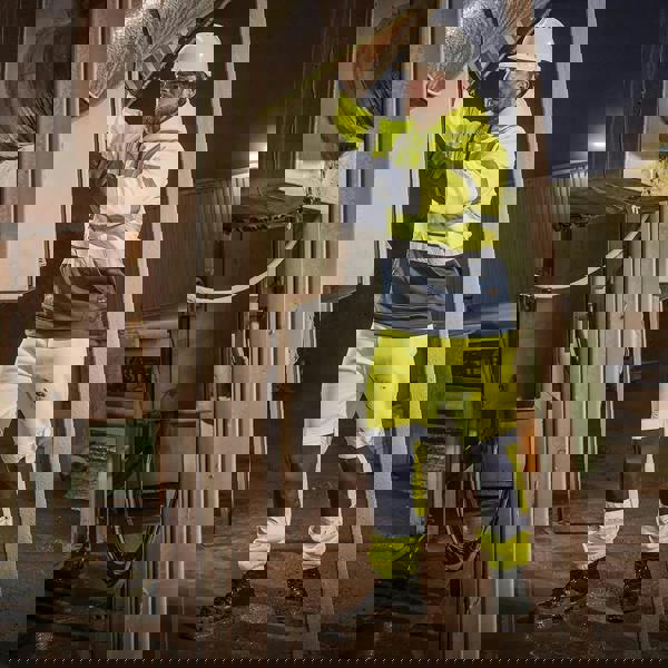 Scruffs High Visibility Mens Hi-Viz Work Pull Over Hoodie, a man working outdoors at night wearing high visibility yellow and navy blue hoodie with reflective strips.