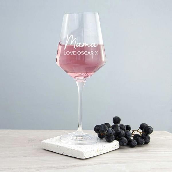 A personalised wine glass for Mum engraved with Mama Love Oscar X filled with rosé wine on a marble coaster.