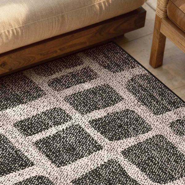 Black and white patterned rug on a wooden floor with a beige sofa and wooden chair.
