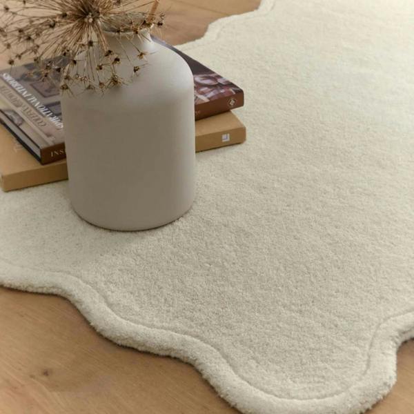 White vase on a textured white rug with books and dried plants.
