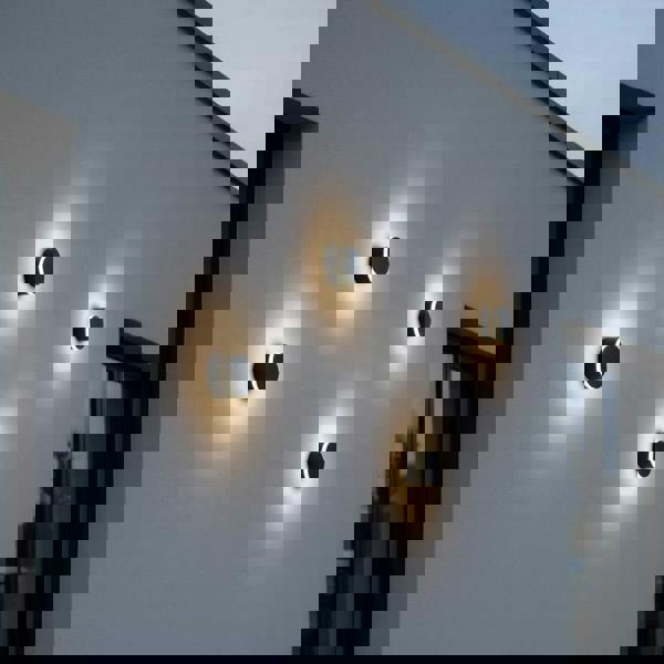 black wall outdoor lamp with 4 lights mounted on the white exterior wall of a modern house 